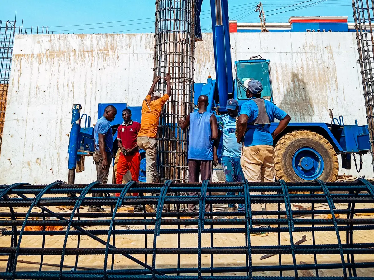Le chantier au matin : la grue dépose les cages d'armature, l'équipe guide la manœuvre.